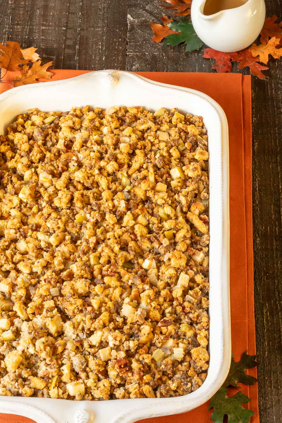 Overhead view of white baking dish holding Sausage Apple Stuffing with Pan Gravy in a pitcher on the side