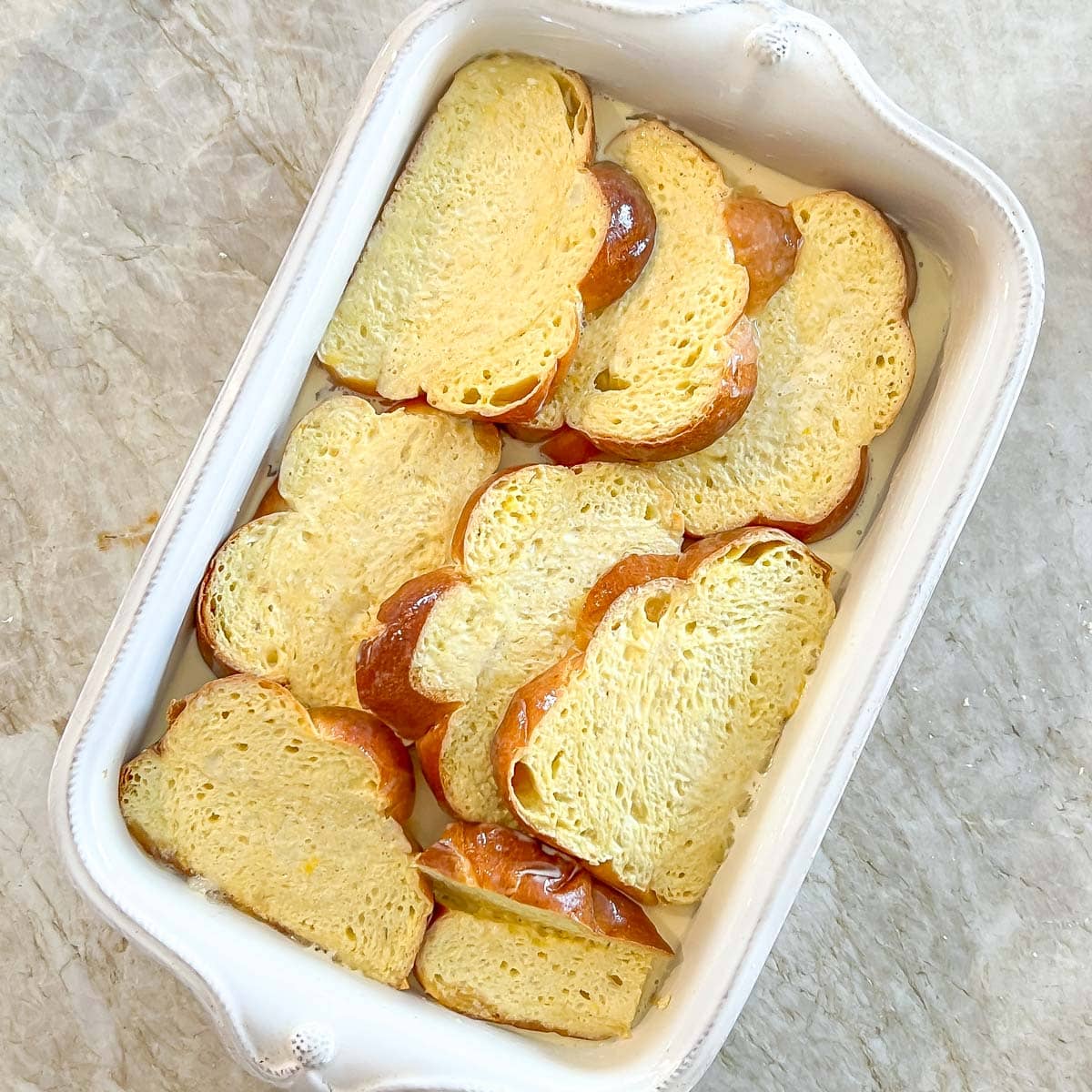 process shot showing bread slices soaked with custard mixture on top of bananas and caramel