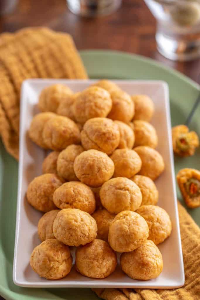 White rectangular platter filled with Olive Cheese Balls. On the right side, two balls are cut in half, showing the olives inside