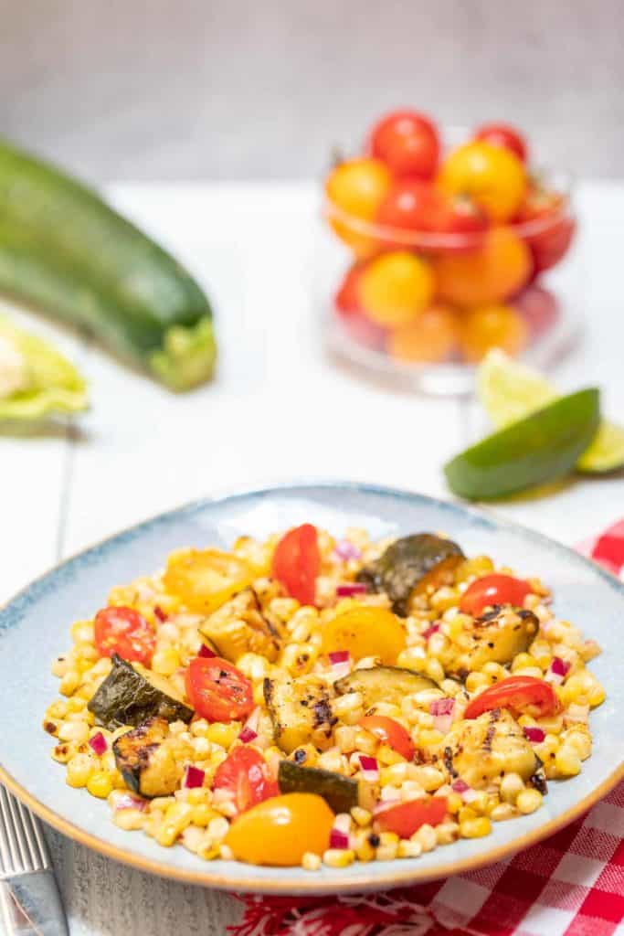 blue bowl holding grilled corn and zucchini salad with tomatoes