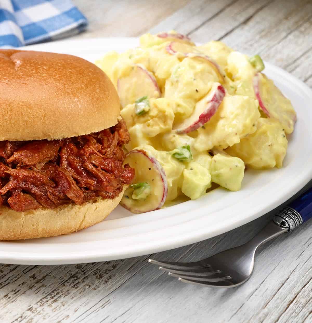 white plate with Dorothy's Potato Salad next to BBQ Beef sandwich
