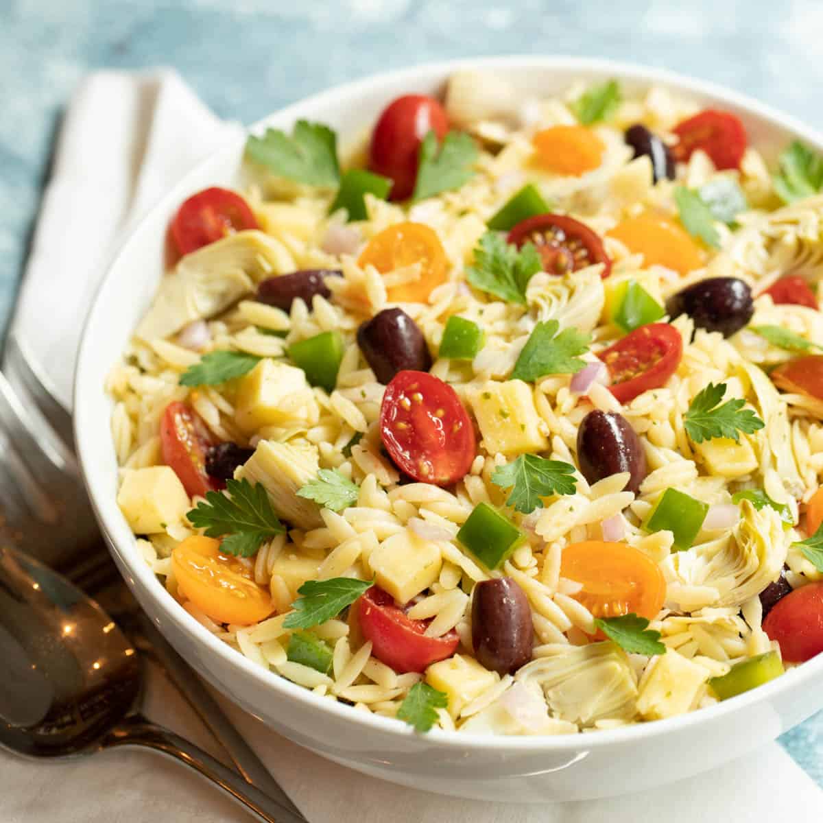 White bowl filled with Greek Orzo Pasta; Lemon-Basil Tahini Dressing is in a glass pitcher on the side