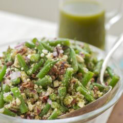glass serving bowl holding green bean salad with mint vinaigrette in a glass pitcher in the back