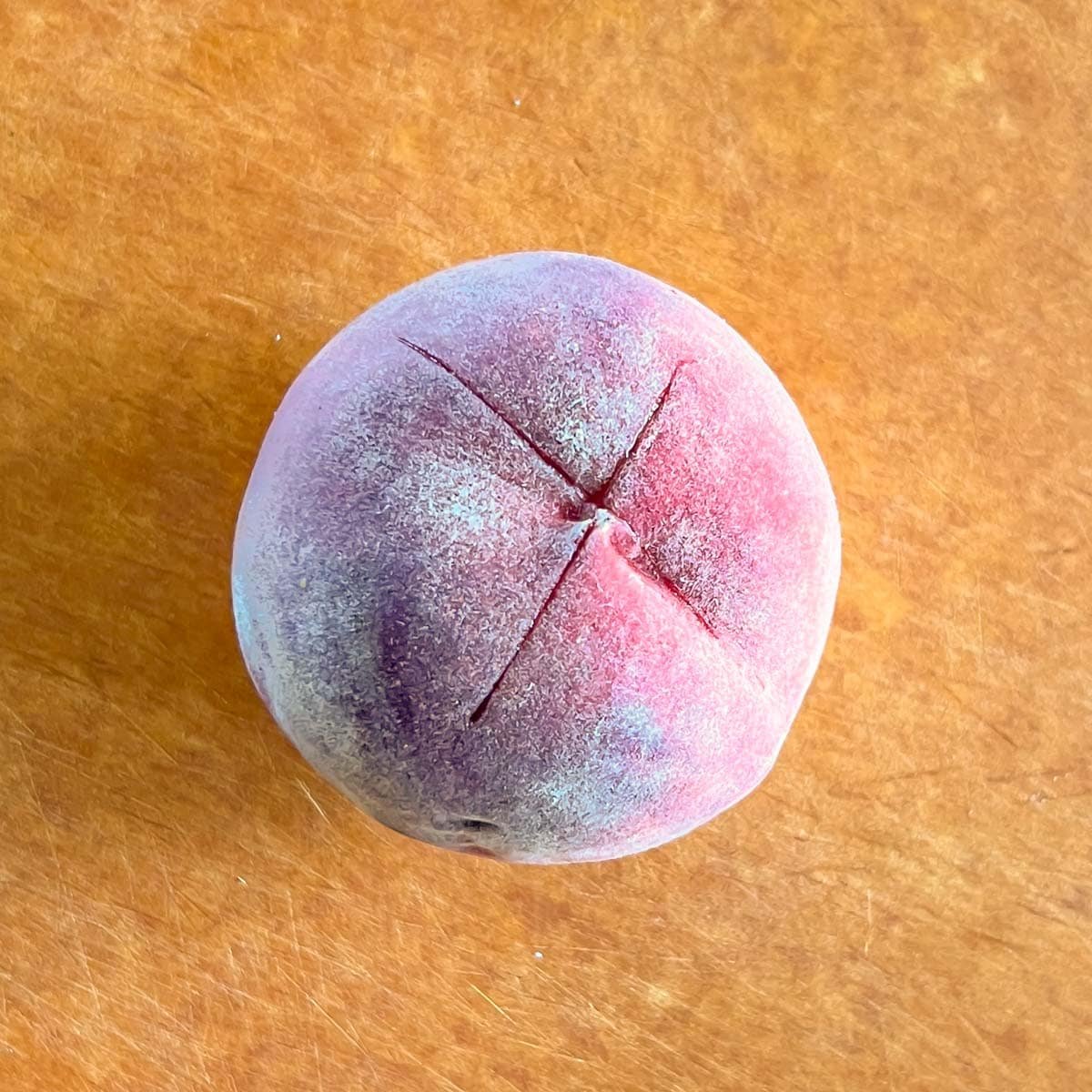 Overhead view of a peach with a shallow “X” through the skin on the bottom. 