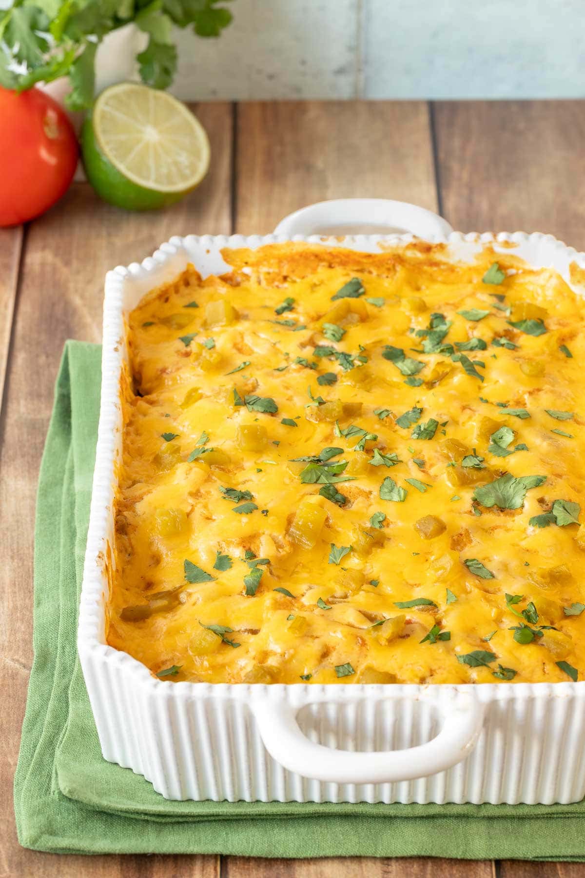 full view of Layered Chicken Enchilada Casserole with lime and tomato in back