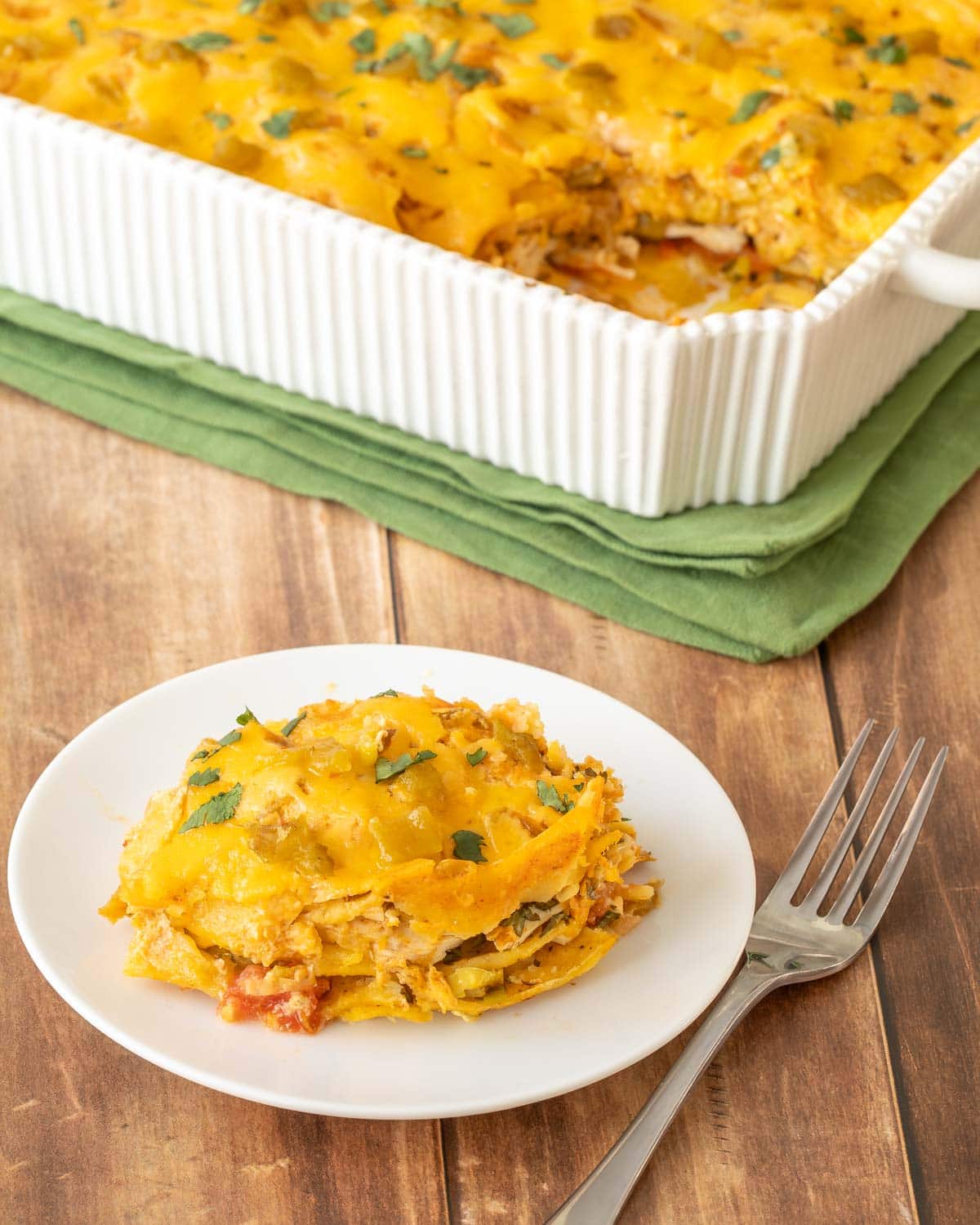 Plate showing a single portion of Layered Chicken Enchilada Casserole, with the remaining casserole in the back