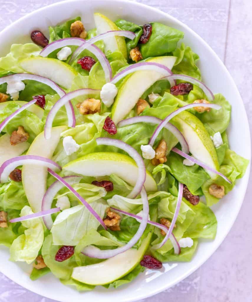 Close up showing Pear and Goat Cheese salad, along with candied walnuts, dried cranberries and sliced red onion