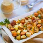 Retangular white platter filled with Roasted Root Vegetables, with a pitcher of mustard sauce on the side
