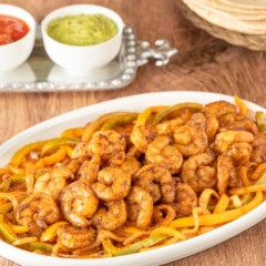 White oval platter holding shrimp fajitas with various toppings and tortillas in the background