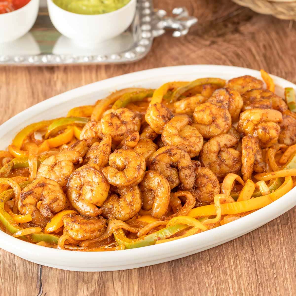 White oval platter holding shrimp fajitas with various toppings and tortillas in the background