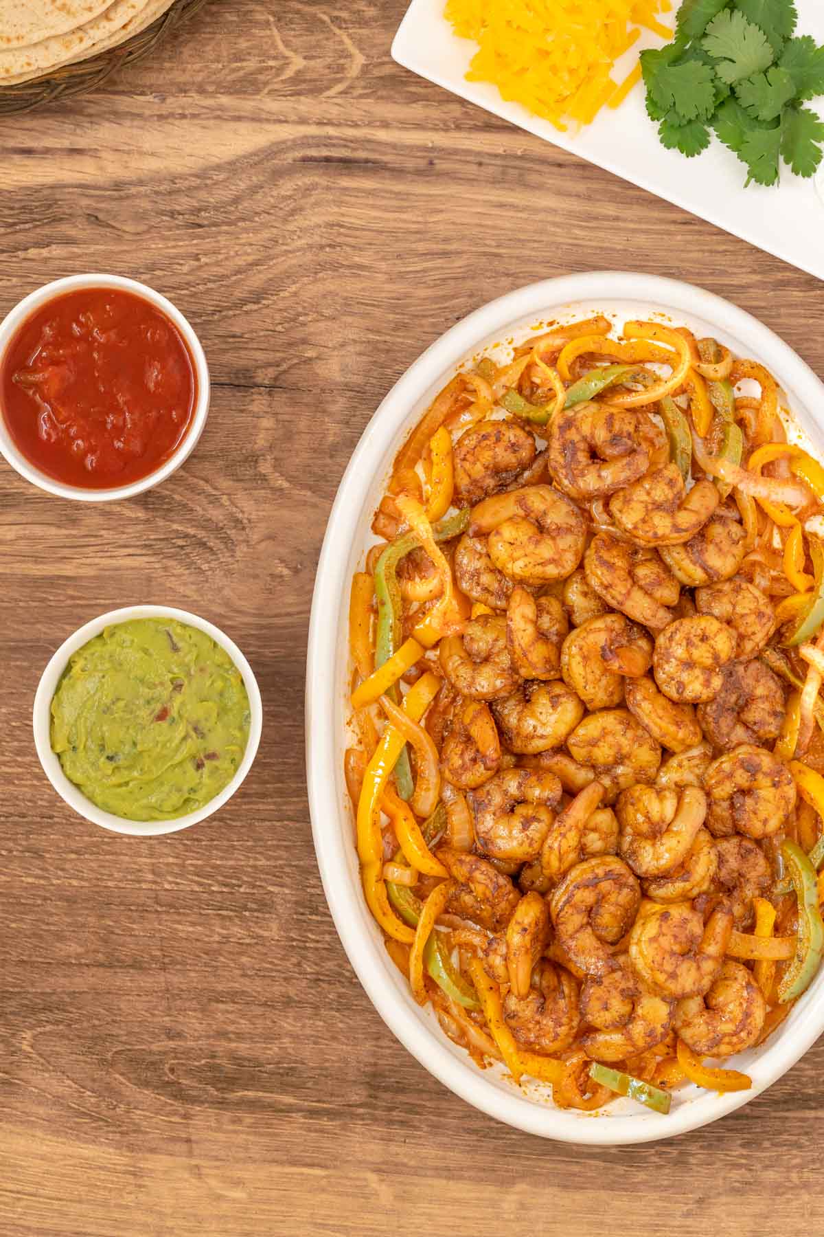 Overhead shot of shrimp fajitas on a white platter with guacamole and salsa on the side