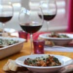White bowl filled with Spinach Farfalle Bolognese, sitting with a glass of red wine