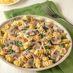 Closer view of a bowl holding a large portion of chicken sausage, spinach, and mushroom pasta, with grated Parmesan