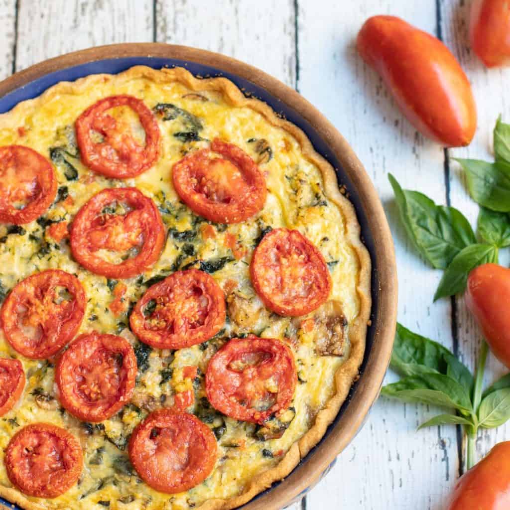 Overhead shot of mushroom, spinach, zucchini pie with sliced tomatoes on top