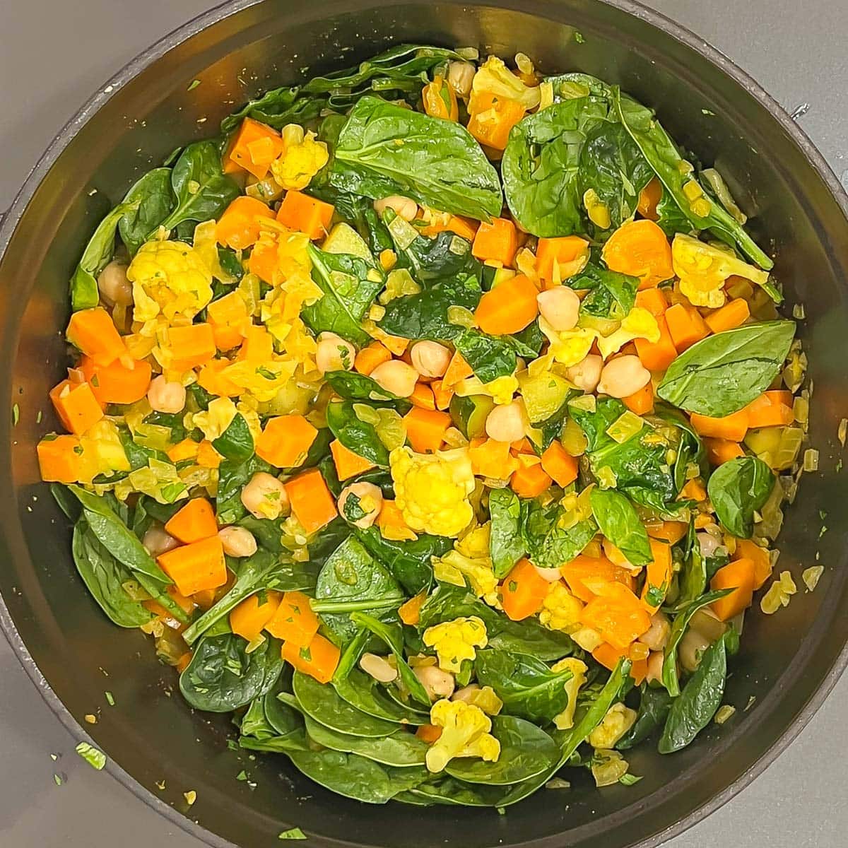 Overhead view of Mixed Vegetable Curry cooking in black pot after spinach and chickpeas are added